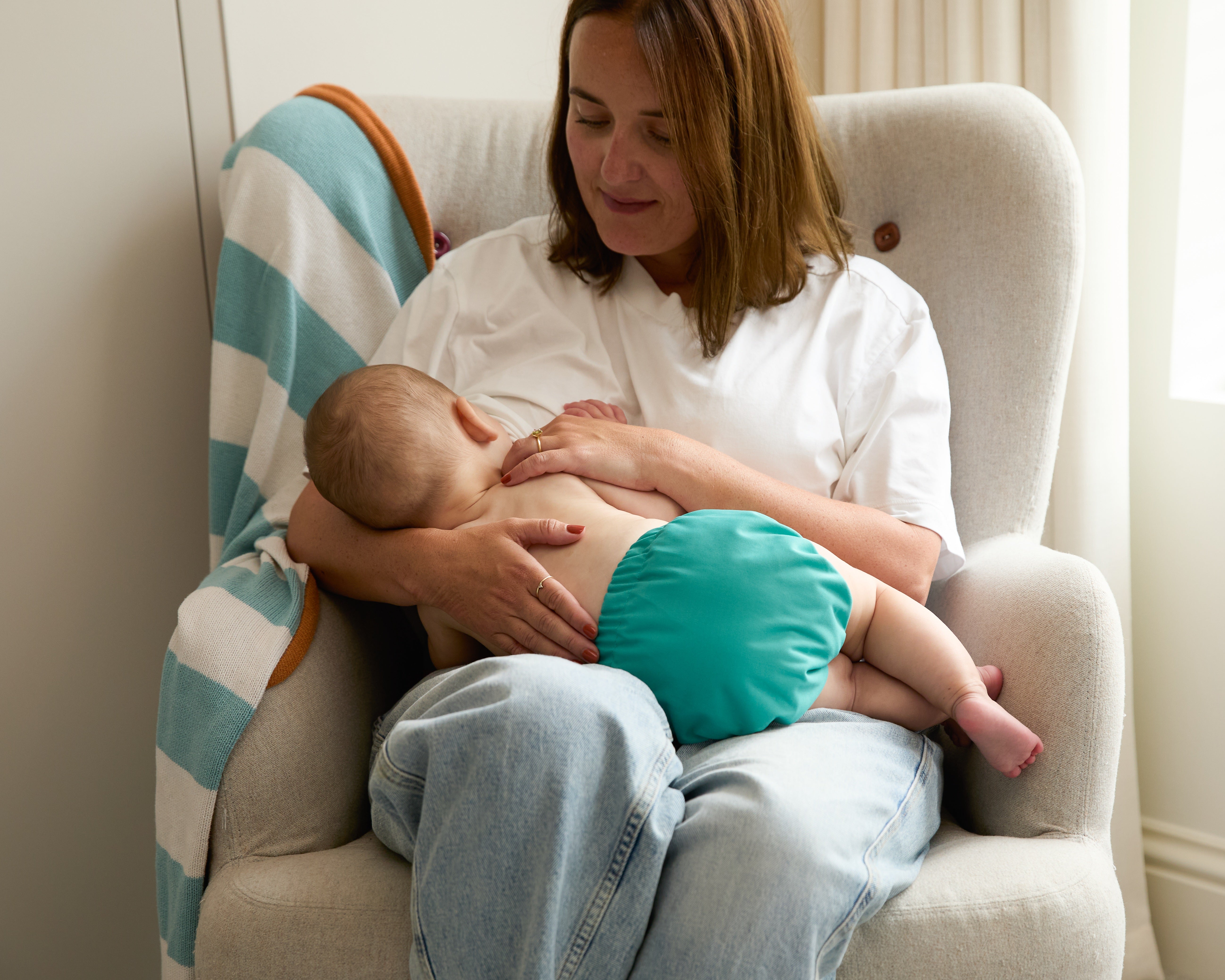 Woman breastfeeding a baby using a pillow on a chair.
