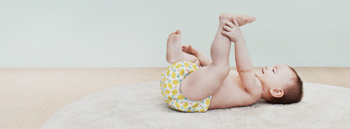 Baby lying on a blanket wearing a colorful diaper against a plain background