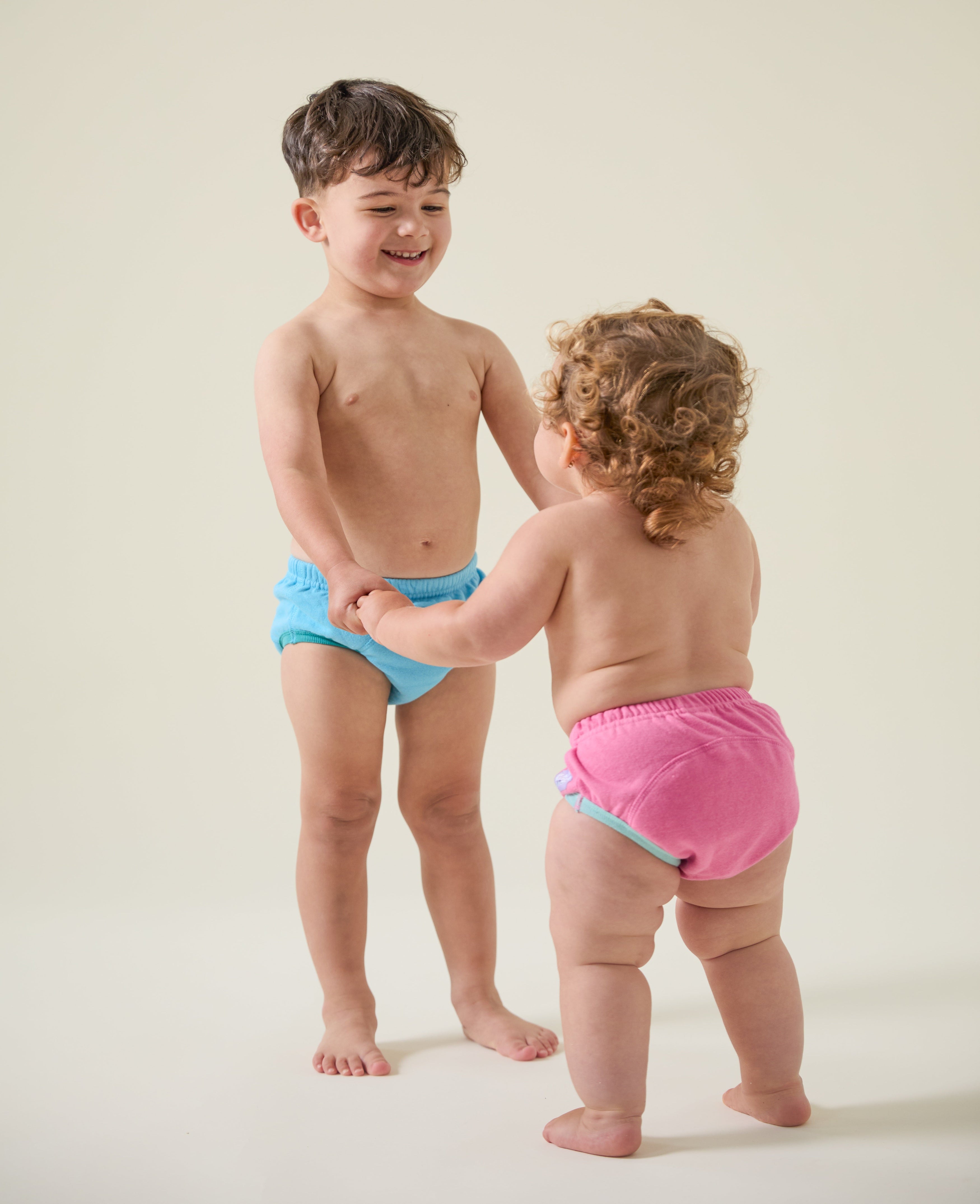 Two children wearing colorful potty training pants on a plain background
