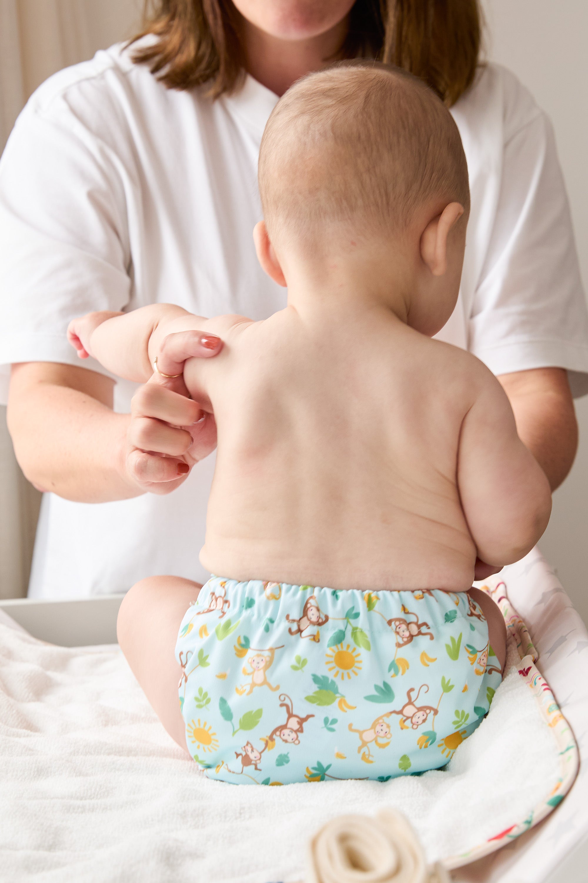 Baby wearing a colorful diaper with a person holding their hand, sitting on a bed.